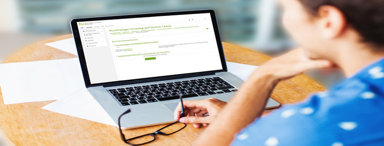 Student sits at workstation and looks at laptop.